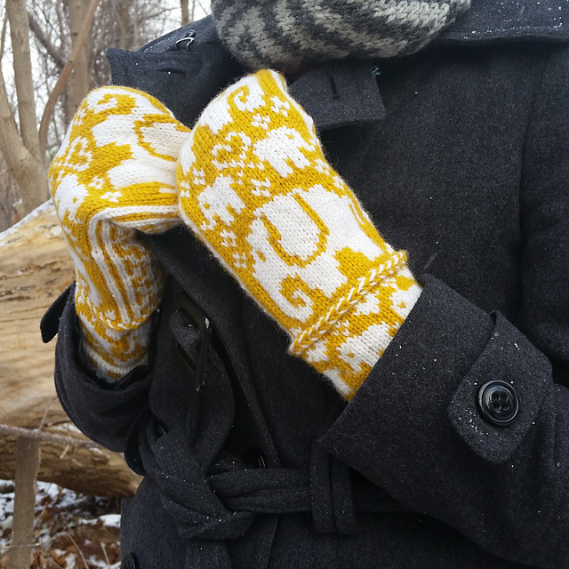 A pair of yellow and white elephant mittens pulling at a jacket collar.
