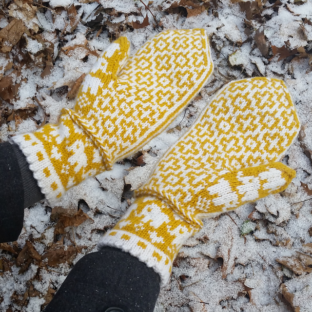 The palms of a yellow and white pair of mittens, featuring a geometric motif and small elephants on the thumbs.