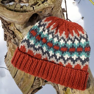 Thick handknit hat with multi-coloured pattern around crown.