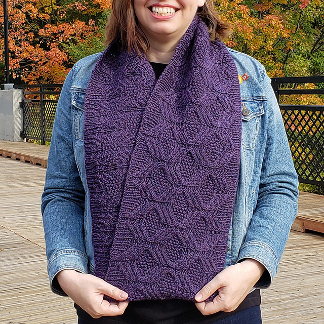 Woman wearing a purple infinity scarf covered in an all over textured cable pattern.