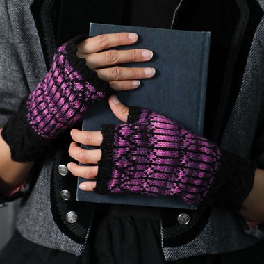 A woman wearing a pair of fingerless mitts, holding a book.